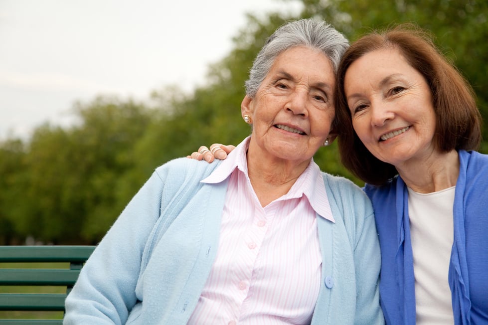 Portrait of an elder mother and daughter sitting on a bench outdoors